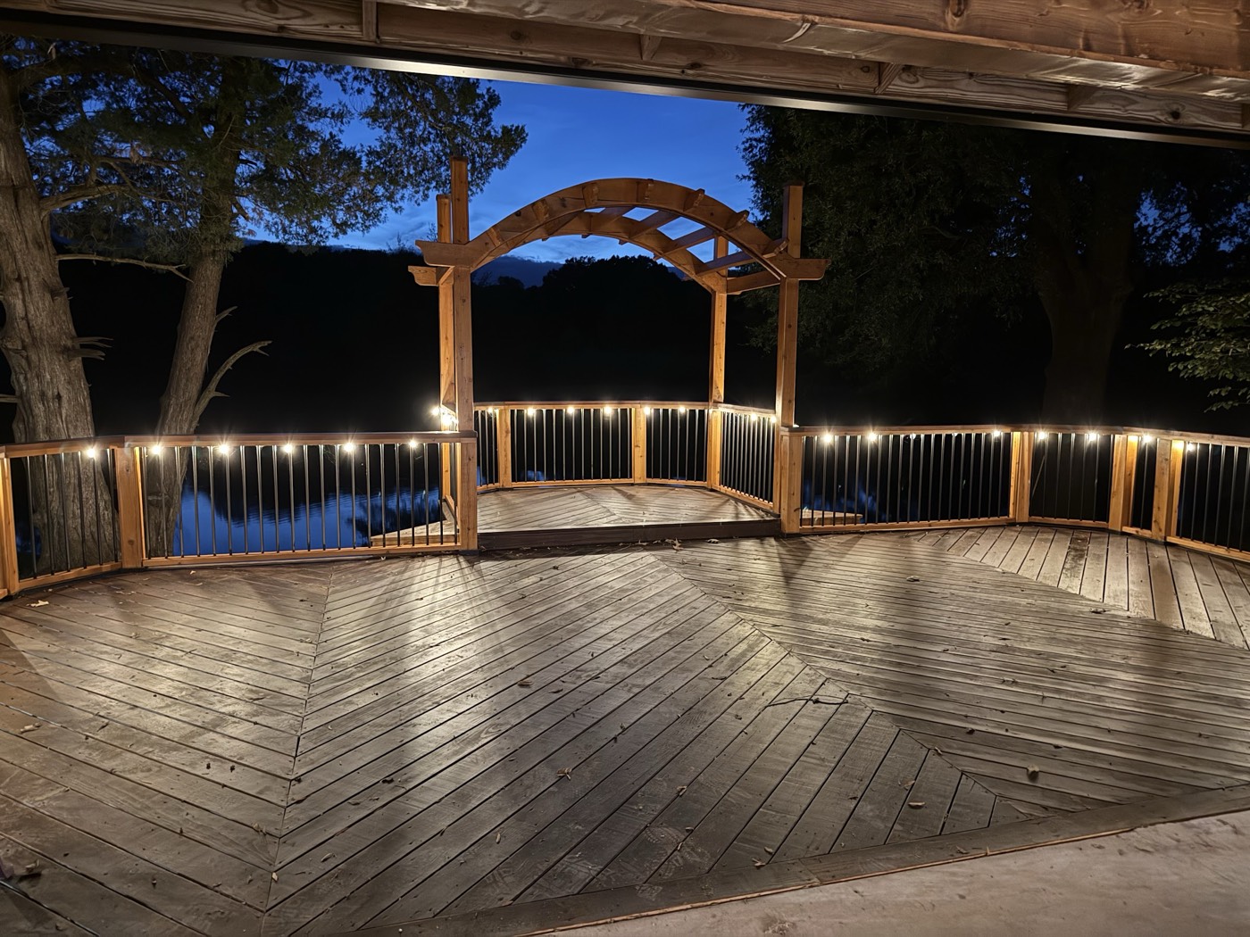 Lit deck and arbor overlooking the pond at night